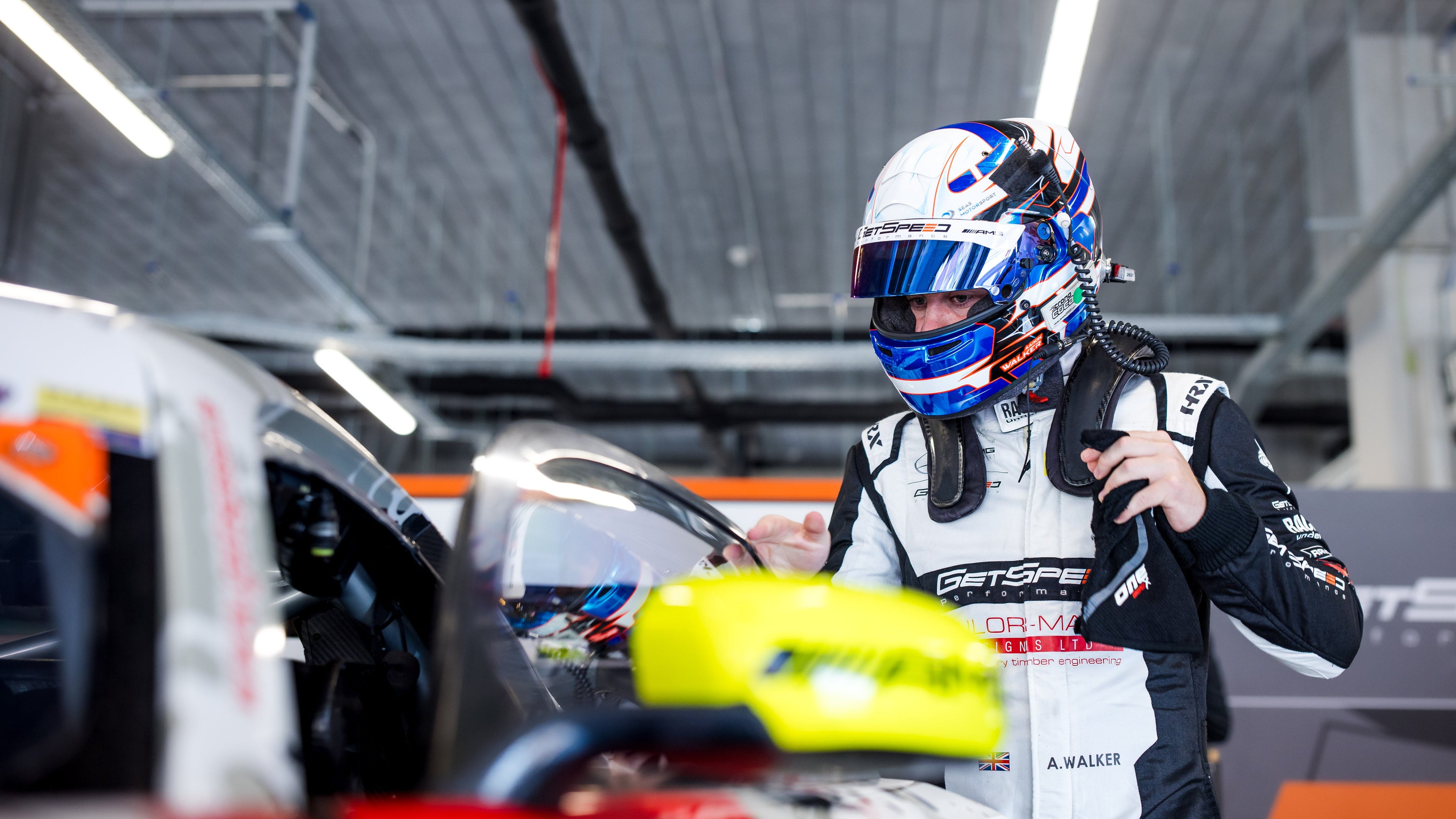 Person in racing gear with helmet and car in foreground